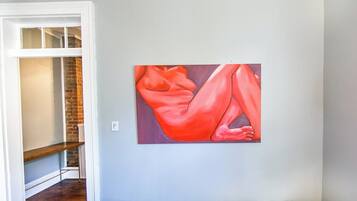 A room with a painting on the wall, a wooden bench, and a brick wall.
