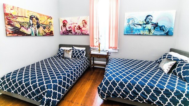 A bedroom with two beds, a nightstand, and three paintings on the wall.