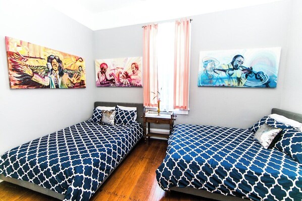 A bedroom with two beds, a nightstand, and three paintings on the wall.