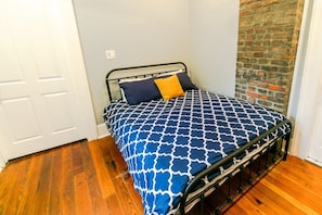 Een eenpersoonsbed met een gebedruid sprei, een bakstenen muur en houten vloer.