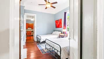 A narrow hallway leading to a bedroom with two beds, a ceiling fan, and a view of a kitchen area.