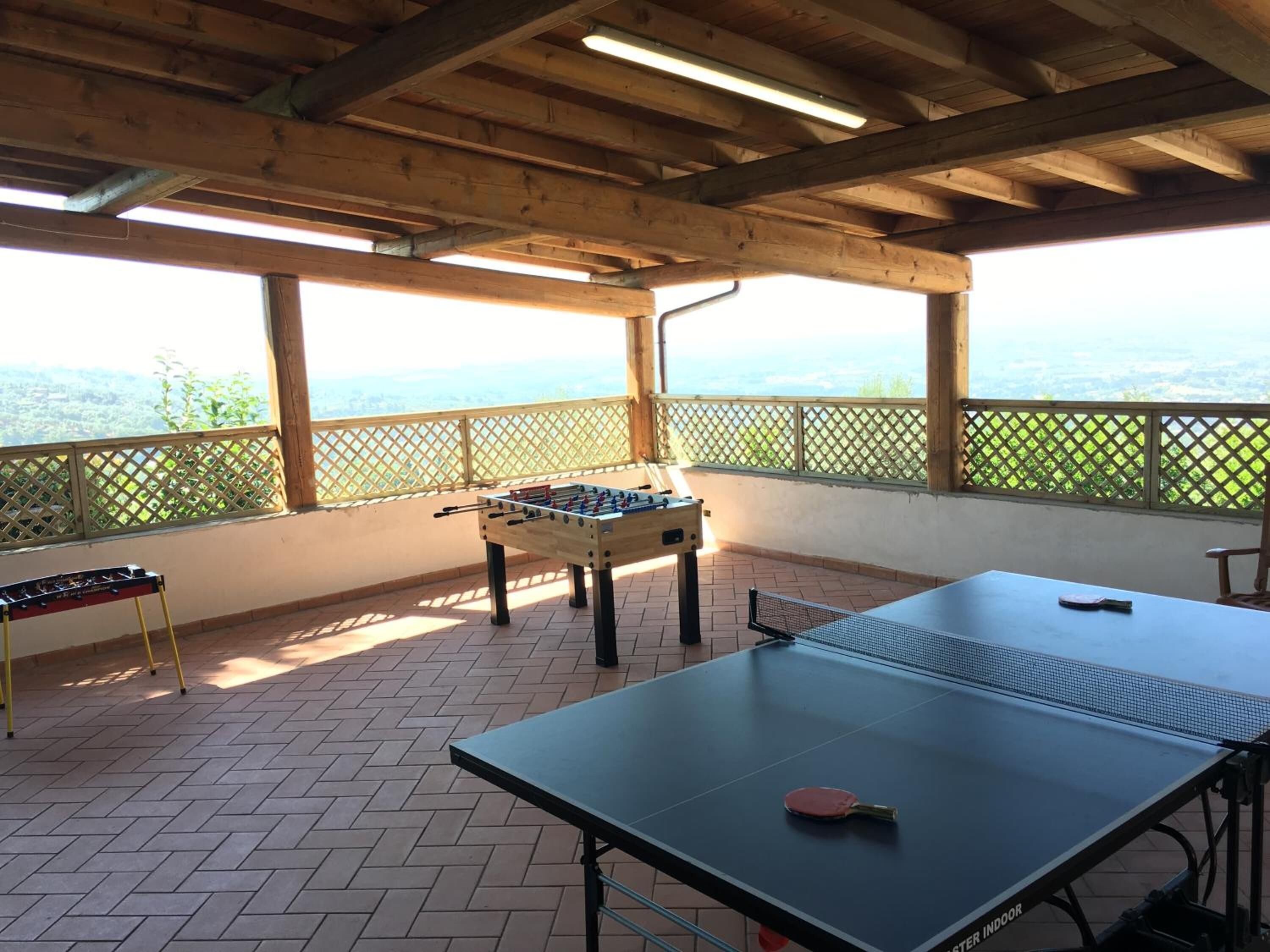 An outdoor area with a foosball table, a ping pong table, and a foosball table with a view of the landscape.