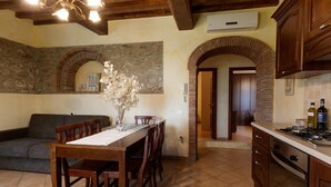 A dining area with a wooden table and chairs, a vase with dried flowers, and a stone wall with an archway. - Borgo dei Gigli (Lamporecchio)