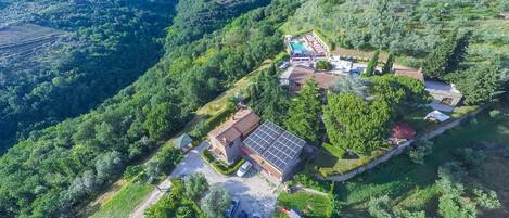 An aerial view of a hillside property with a swimming pool, a solar panel-equipped building, and a small guesthouse.
