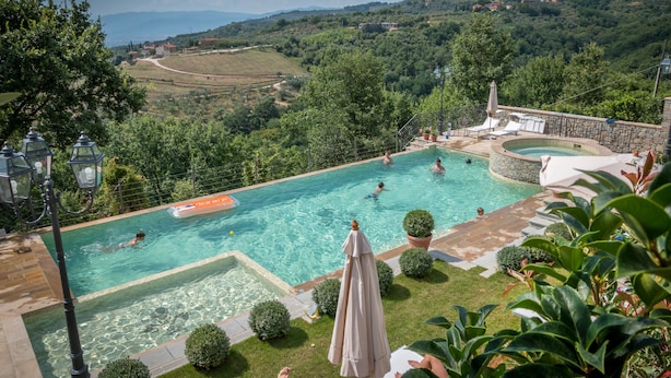A swimming pool with clear water, surrounded by lush greenery and a stone wall. - Borgo dei Gigli (Lamporecchio)