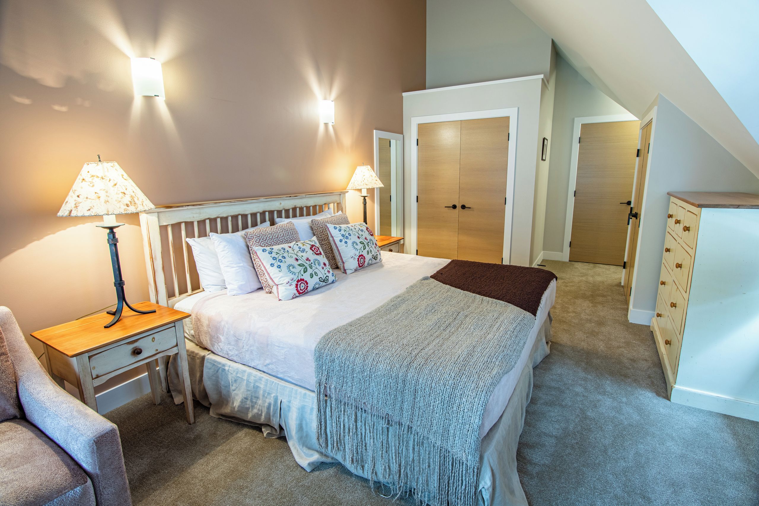 A bedroom with a bed, bedside tables, lamps, a dresser, and a closet.