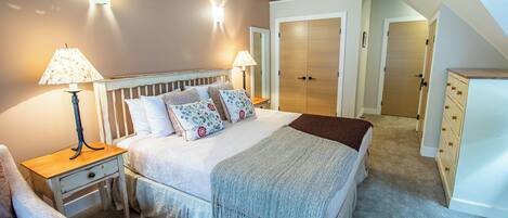 A bedroom with a bed, bedside tables, lamps, a dresser, and a closet.