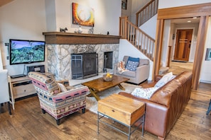 A living room with a stone fireplace, a television, a sofa, a coffee table, and a patterned armchair. - Pinnacle Ridge 36 - Ski in Ski out, Private Hot Tub, Wood Fireplace (Whistler)