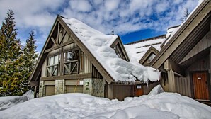 Un chalet en bois doté d’un toit à forte pente recouvert de neige, de grandes fenêtres et d’une façade en pierre.