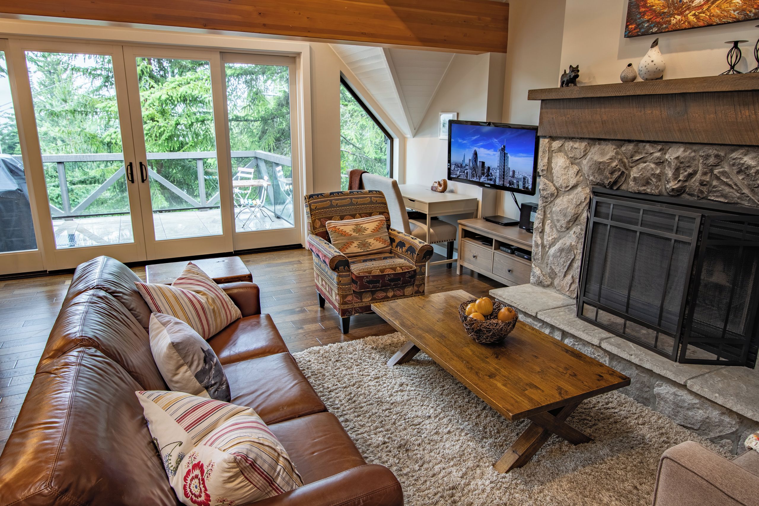 A spacious living room with a leather sofa, a patterned armchair, a wooden coffee table, and a stone fireplace.