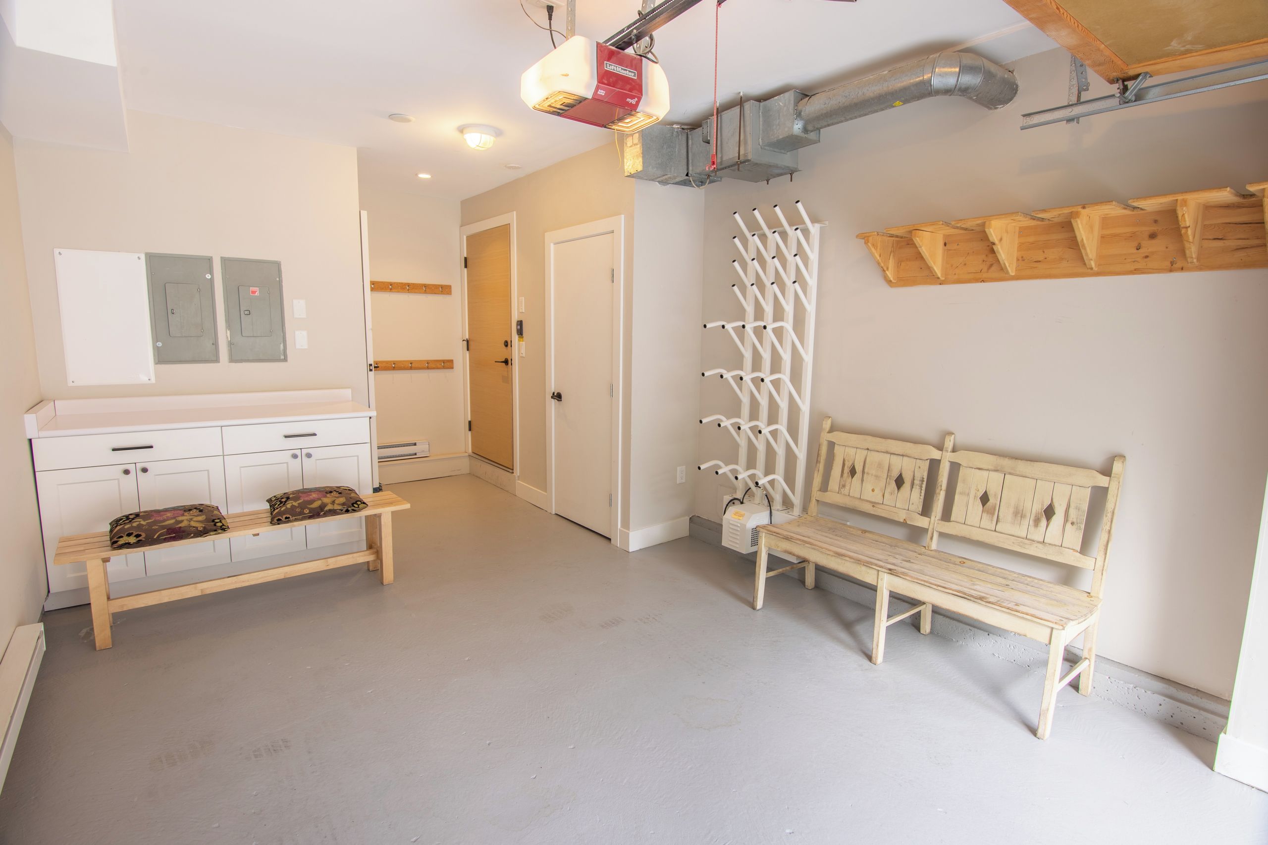 Une cuisine propre et moderne, avec des meubles blancs, un banc en bois et un autre banc blanc adossé au mur.