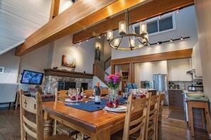 A dining area with a wooden table set for a meal, a chandelier, and a stone fireplace.