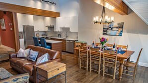 Une cuisine moderne avec des meubles blancs, un réfrigérateur en acier inoxydable et un coin repas comprenant une table et des chaises en bois.