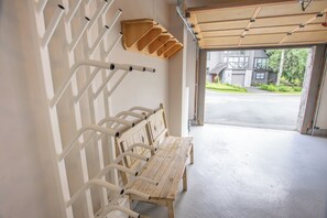 A clean, modern interior with a wooden bench and white metal railings, leading to a garage with a view of a residential area. - Pinnacle Ridge 36 - Ski in Ski out, Private Hot Tub, Wood Fireplace (Whistler)