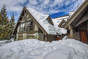A wooden lodge with a steeply pitched roof covered in snow, large windows, and a stone facade. - Pinnacle Ridge 36 - Ski in Ski out, Private Hot Tub, Wood Fireplace (Whistler)
