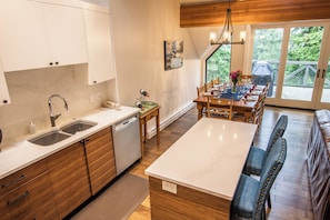 A modern kitchen with wooden cabinets, a dishwasher, and a dining area with a table set for four. - Pinnacle Ridge 36 - Ski in Ski out, Private Hot Tub, Wood Fireplace (Whistler)