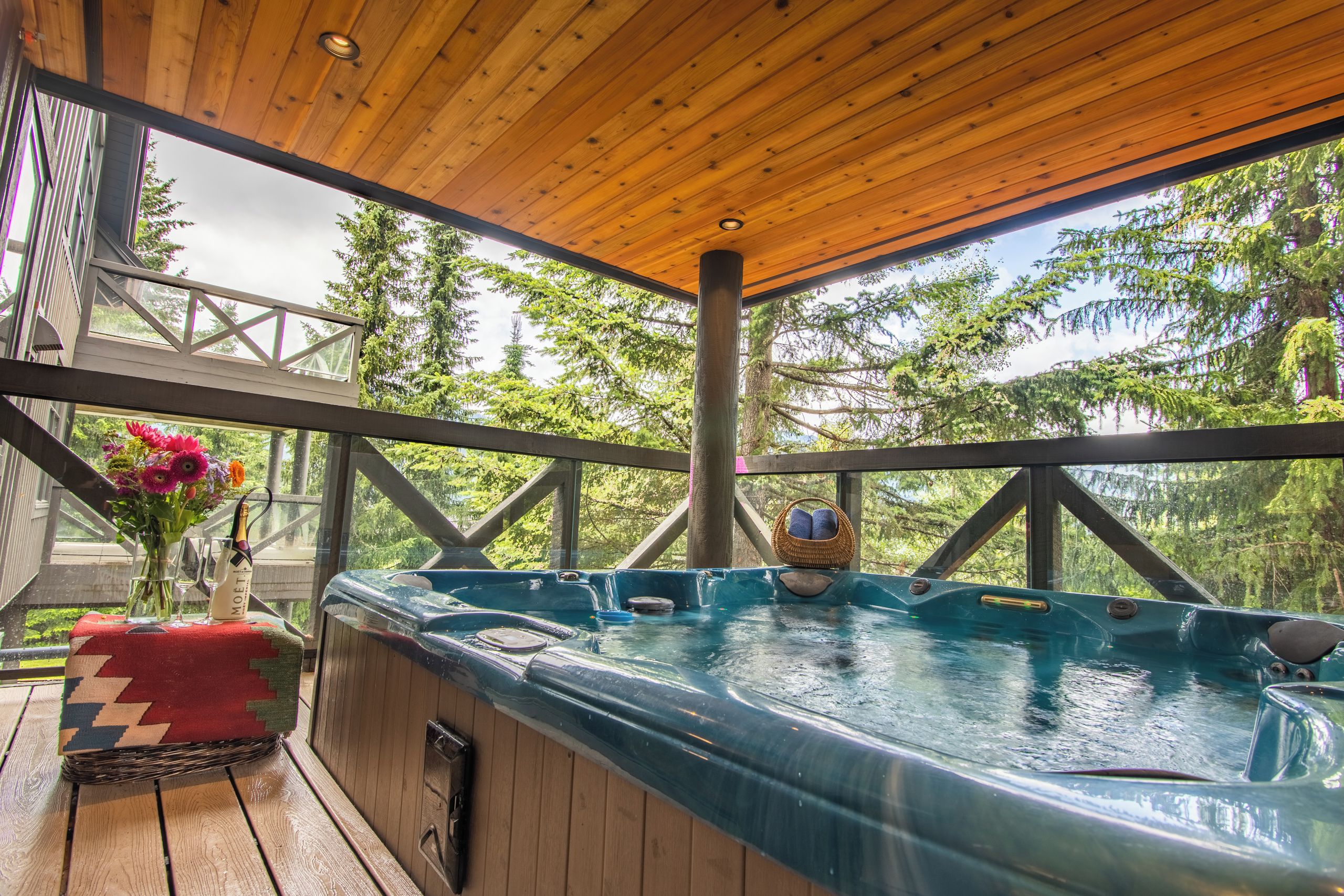 A wooden deck with a hot tub, a wicker basket, and a vase with flowers.