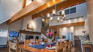Un coin repas avec une table en bois dressée pour le repas, un lustre et une cheminée en pierre.