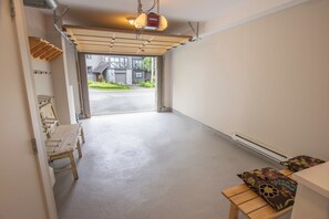 A garage with a wooden bench and a table, a ceiling light, and a view of a house through the open garage door. - Pinnacle Ridge 36 - Ski in Ski out, Private Hot Tub, Wood Fireplace (Whistler)