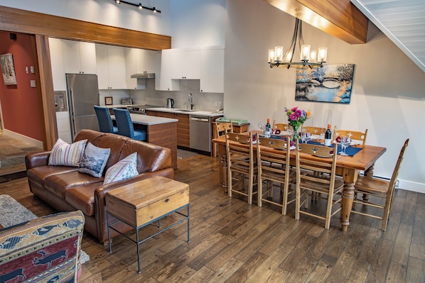 A modern kitchen with white cabinets, a stainless steel refrigerator, and a dining area with a wooden table and chairs. - Pinnacle Ridge 36 - Ski in Ski out, Private Hot Tub, Wood Fireplace (Whistler)