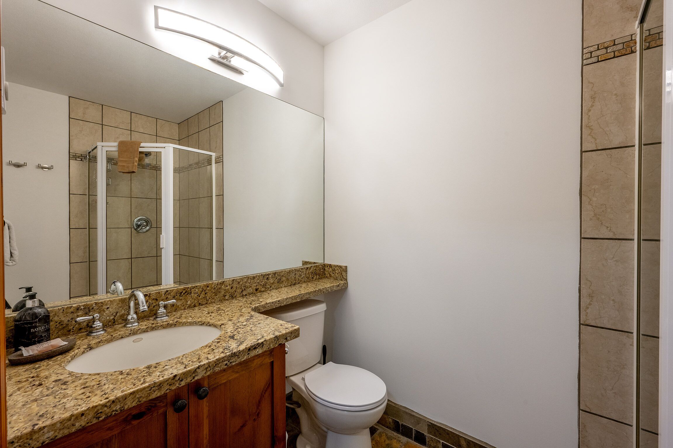 A bathroom with a granite countertop sink, a mirror, a toilet, and a shower enclosure.