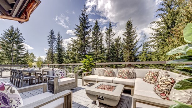An outdoor deck with a sofa, chairs, and a table, surrounded by tall trees and a clear sky. - Pinnacle Ridge 5 - Ski in Ski out, Private Hot Tub, Gas Fireplace (Whistler)