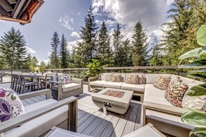 An outdoor deck with a sofa, chairs, and a table, surrounded by tall trees and a clear sky.