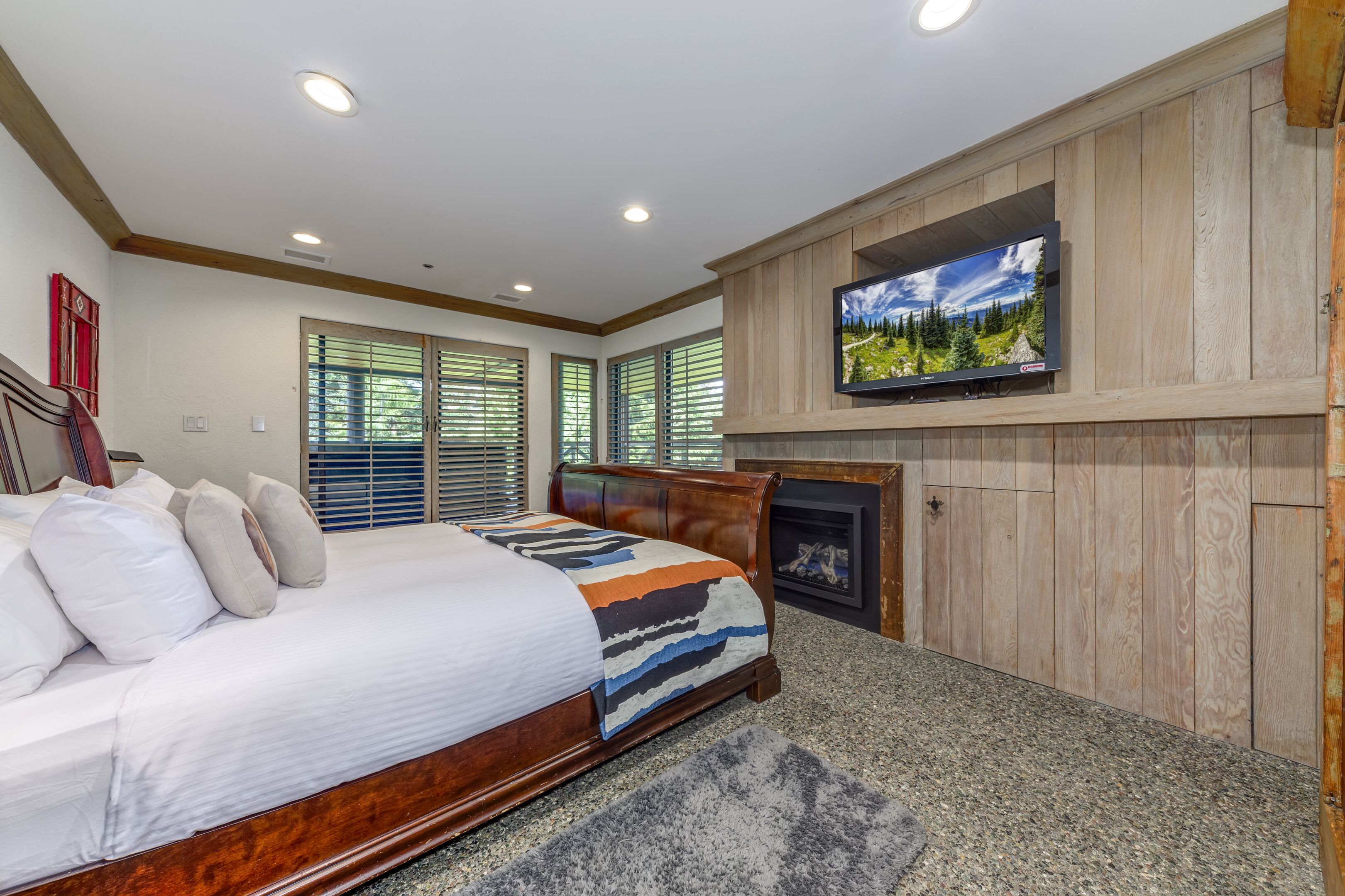 A bedroom with a bed, a fireplace, a television, and wooden paneling.