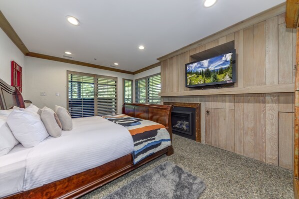 A bedroom with a bed, a fireplace, a television, and wooden paneling.