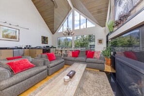 A spacious living area with a high ceiling, large windows, and a modern kitchen. - Pinnacle Ridge 5 - Ski in Ski out, Private Hot Tub, Gas Fireplace (Whistler)