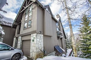 A two-story wooden cabin with a stone foundation, a garage, and a staircase leading to the upper floor. - Pinnacle Ridge 5 - Ski in Ski out, Private Hot Tub, Gas Fireplace (Whistler)