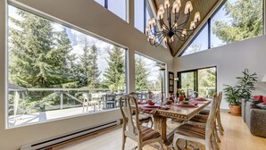 A dining area with a large table, chairs, and a view of trees through large windows. - Pinnacle Ridge 5 - Ski in Ski out, Private Hot Tub, Gas Fireplace (Whistler)