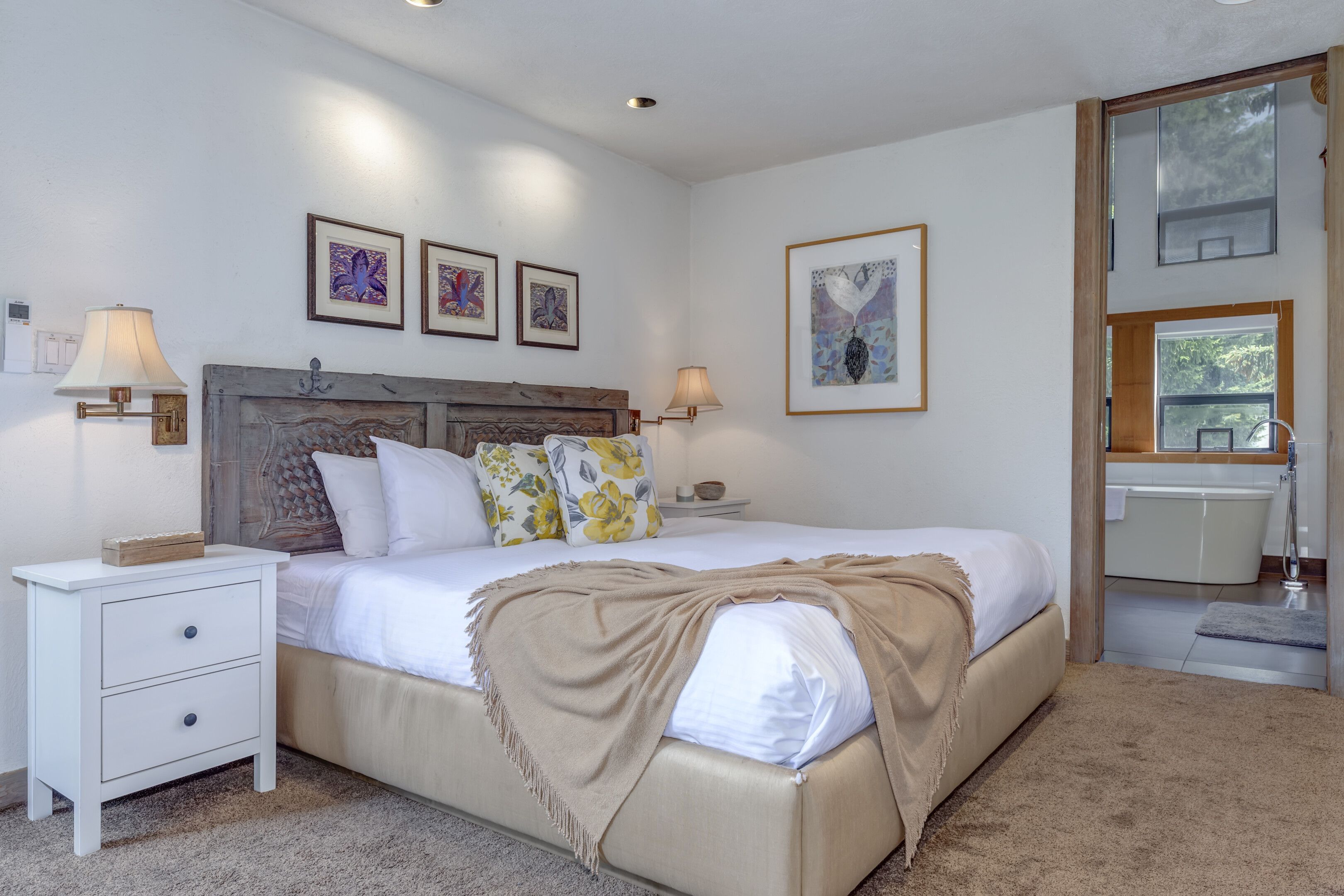 Une chambre à coucher comprenant un lit, des tables de chevet, une commode, une fenêtre et des œuvres d’art accrochées aux murs.
