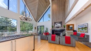 A spacious living area with a kitchen island, grey sofas with red cushions, a fireplace, and large windows offering a view of the outdoors. - Pinnacle Ridge 5 - Ski in Ski out, Private Hot Tub, Gas Fireplace (Whistler)