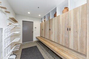 A hallway with a grey door, a bench, and wooden lockers with handles.