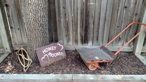 Ein Holzzaun, ein Schubkarren und ein Schild mit der Aufschrift 'HONEY MOONERS'.