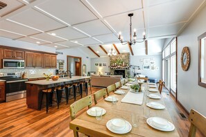 Una cocina amplia con una isla grande, taburetes de bar de madera y una zona de comedor preparada para seis personas.