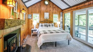 Ein gemütliches Blockhauszimmer mit einem Bett, einem Kamin und einem großen Fenster mit Blick auf eine Terrasse.