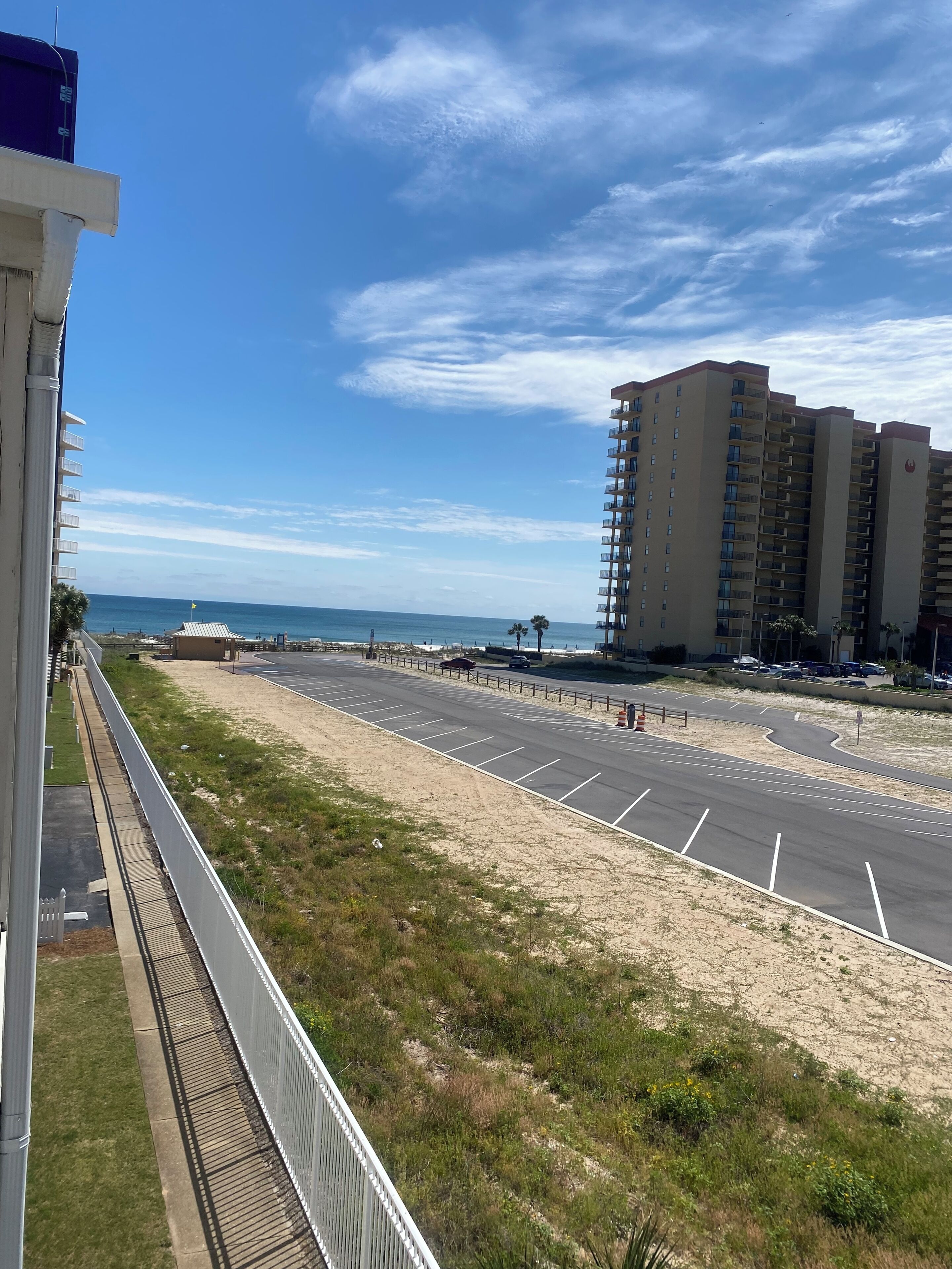 Eine Küstenstraße mit Parkplatz, Strand und Hochhäusern im Hintergrund.