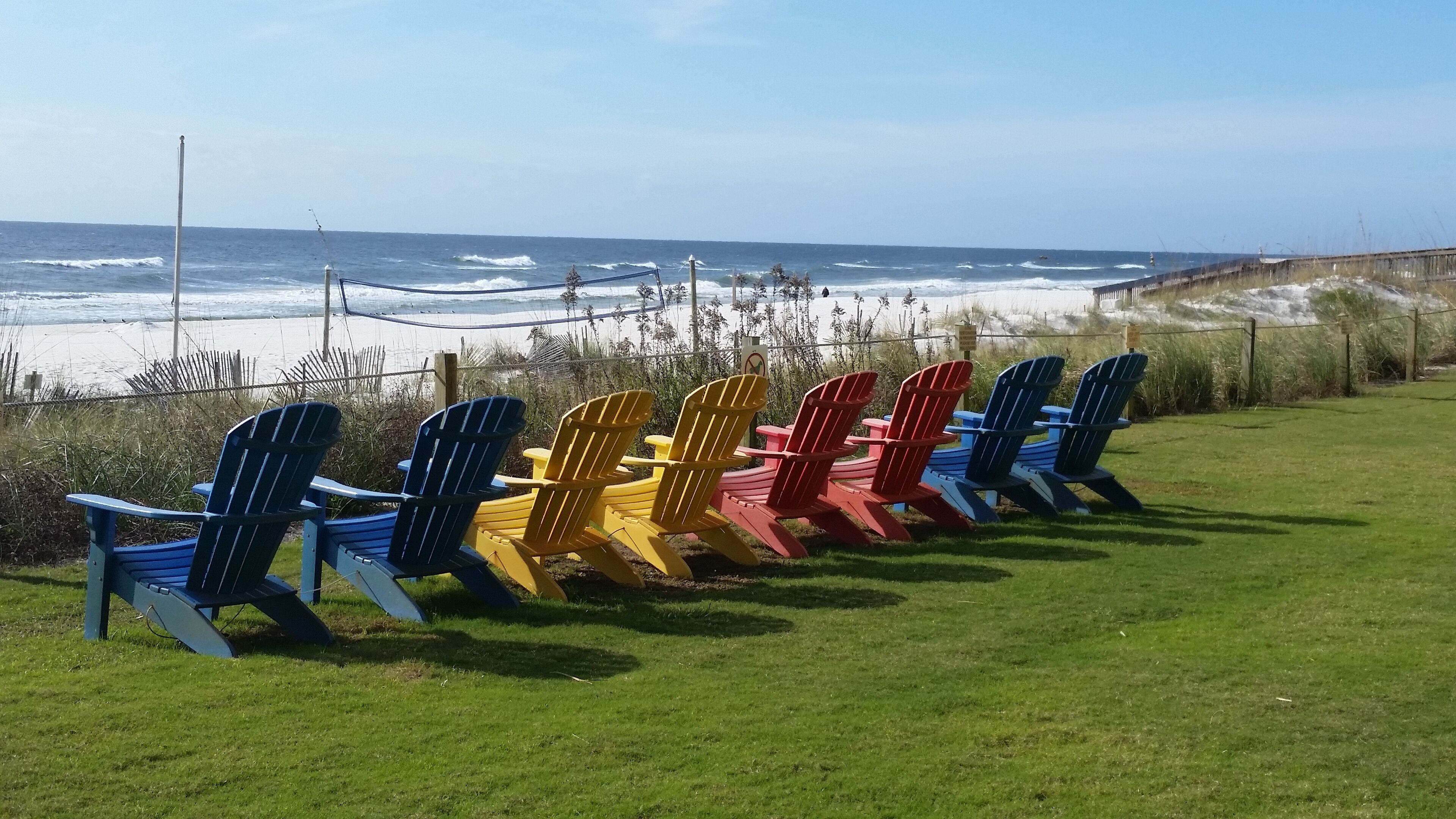 Eine Reihe bunter Adirondack-Stühle mit Blick auf einen Strand und Wellen.