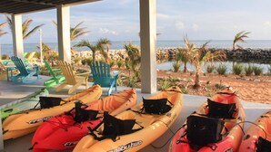 A covered area with kayaks and beach chairs, overlooking a rocky beach and the sea. - Oceanfront Home on Deep Water Canal w/Dock, Pool, Hot Tub, Kayaks, Pool Table! (Marathon)