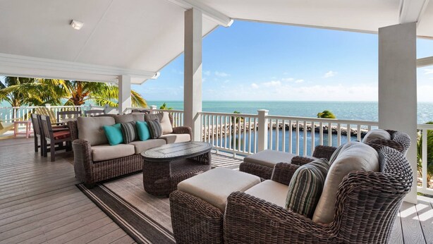 A covered outdoor seating area with wicker furniture and a view of the ocean. - Oceanfront Home on Deep Water Canal w/Dock, Pool, Hot Tub, Kayaks, Pool Table! (Marathon)