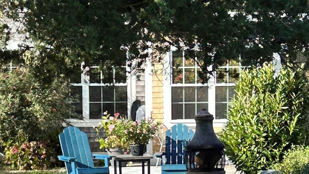 A patio area with blue Adirondack chairs, a table, and a black grill.