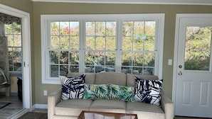 A beige sofa with patterned cushions in front of a bay window with a view of trees.