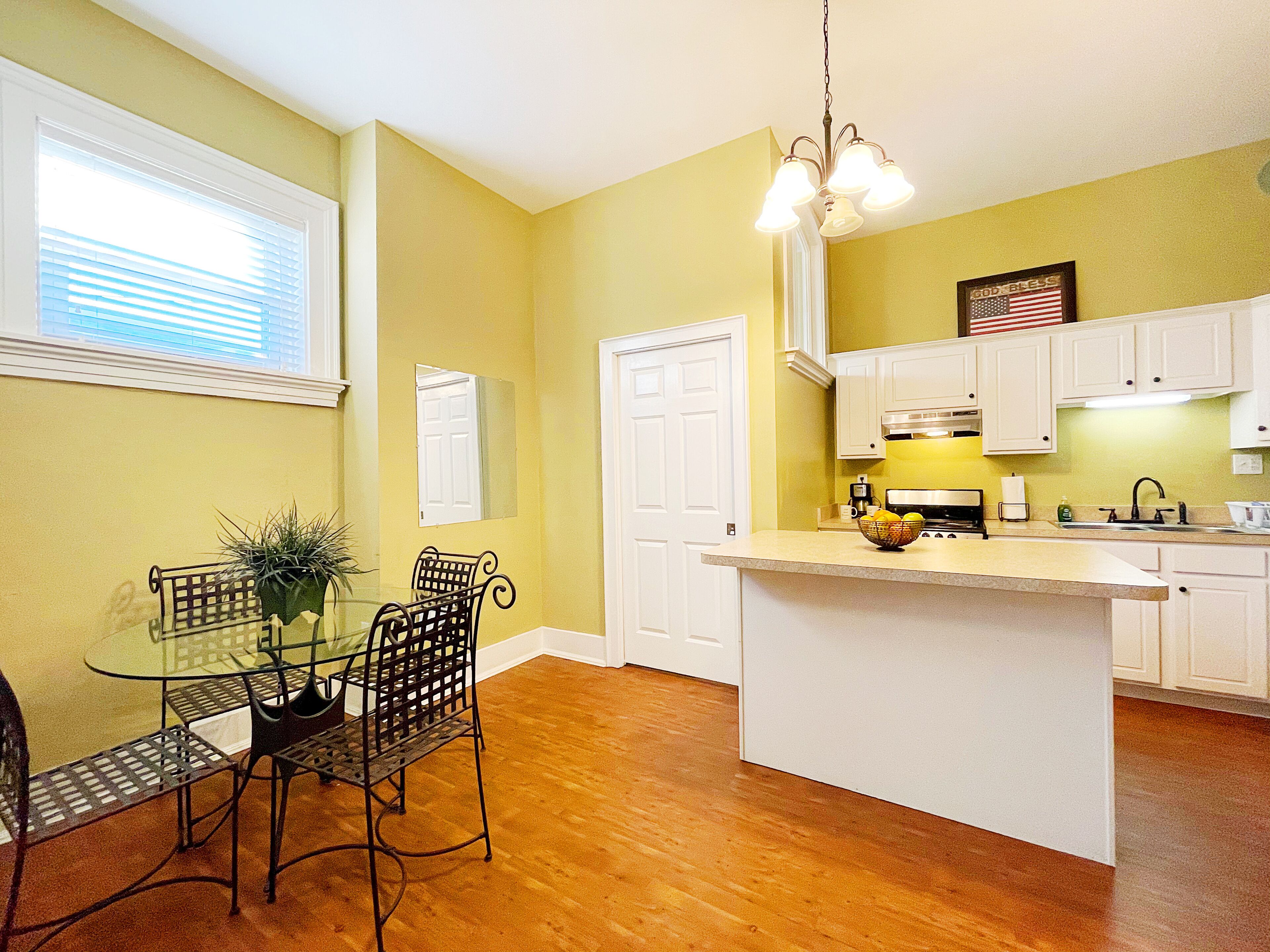 A kitchen with a central island, white cabinets, and a dining area with a glass table and chairs.