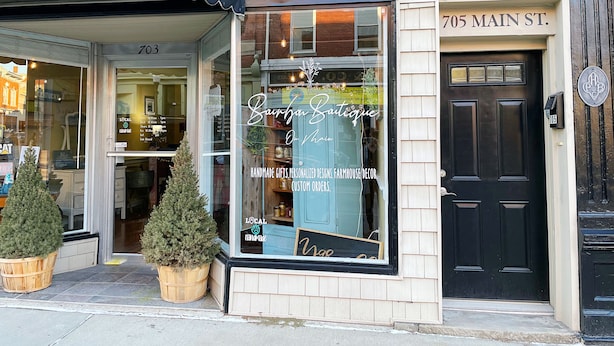 Una botiga amb un gran finestral que mostra 'Sapphire Boutique' i 'Regals artesanals, dissenys personalitzats, decoració rústica, comandes a mida'. El número '705 Main St.' es veu sobre la porta.