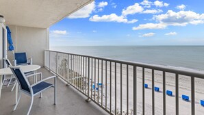 Un balcon donnant sur la plage, avec des chaises blanches et une balustrade.
