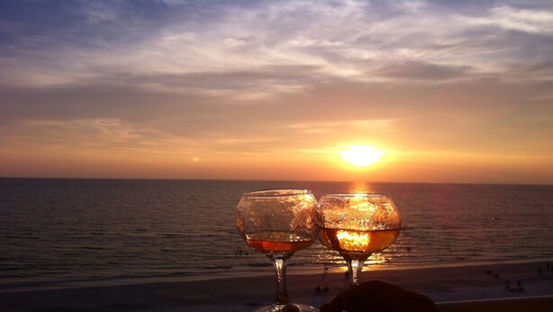 Deux verres de vin sur un balcon donnant sur un coucher de soleil sur l’océan.