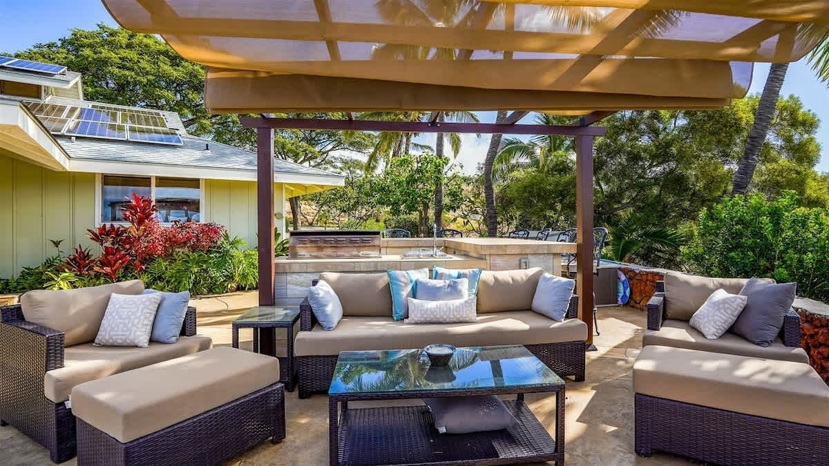 An outdoor patio with wicker furniture, a glass table, and a pergola.