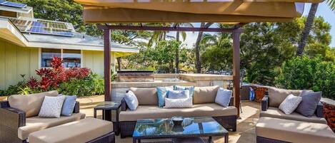 An outdoor patio with wicker furniture, a glass table, and a pergola.